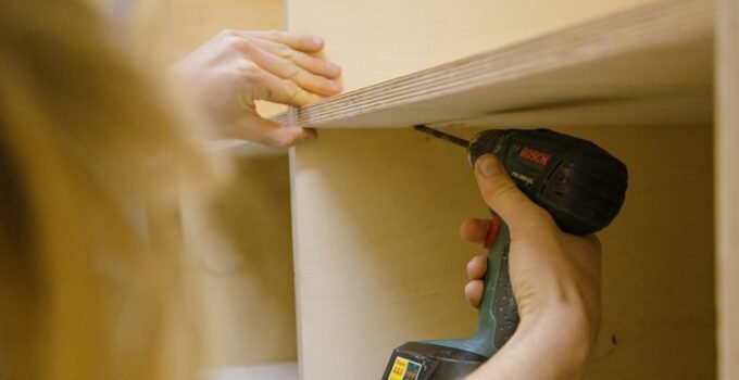 Installer fixing a plywood cabinet shelf with a cordless drill during a kitchen cabinet installation