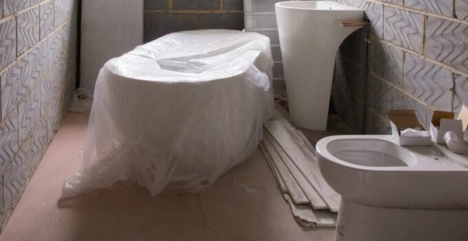 Small bathroom remodel in progress with fixtures wrapped and subfloor exposed